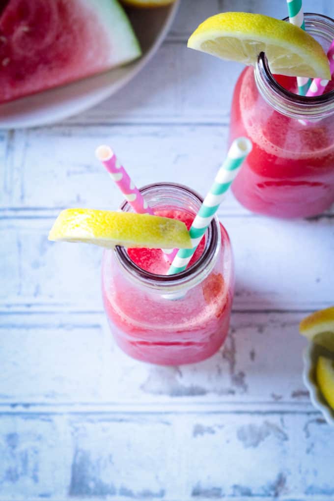Overhead view of a glass of watermelon juice topped with a lemon slice and two straws.