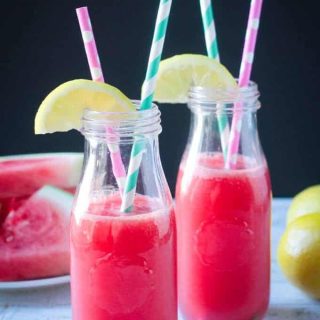 Two glass bottles of watermelon juice with straws and lemon wedges on top.