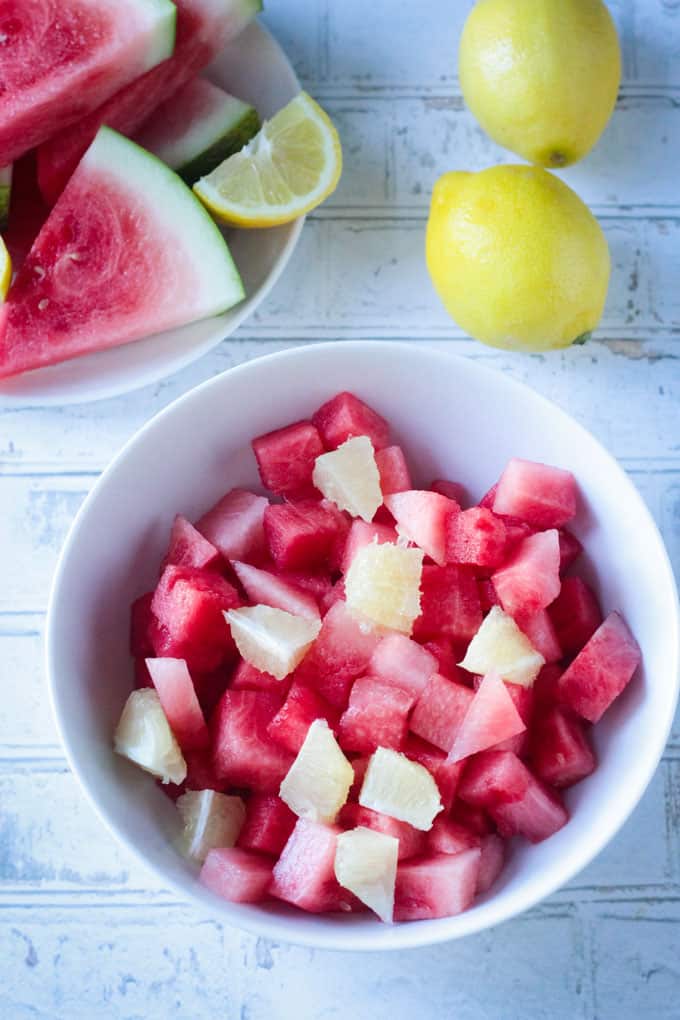 Bowl of watermelon cubes and lemon wedges.