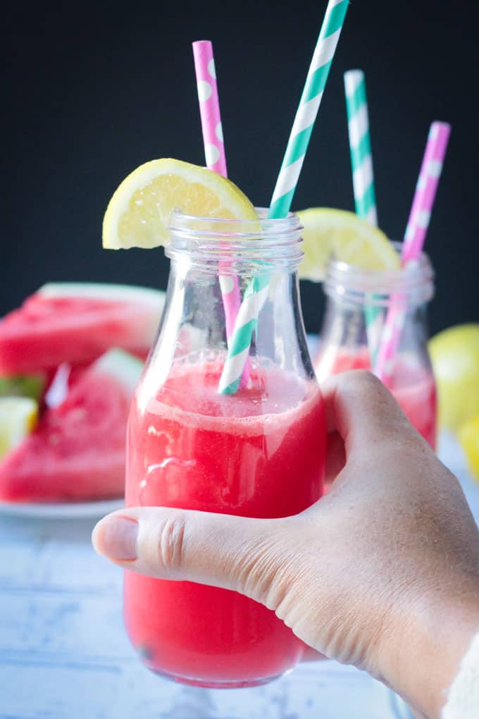 Hand holding up a glass of watermelon juice.