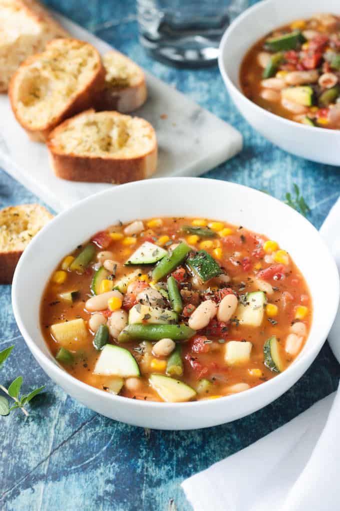 Close up of a white bean soup recipe with green beans, tomatoes, zucchini, and corn.