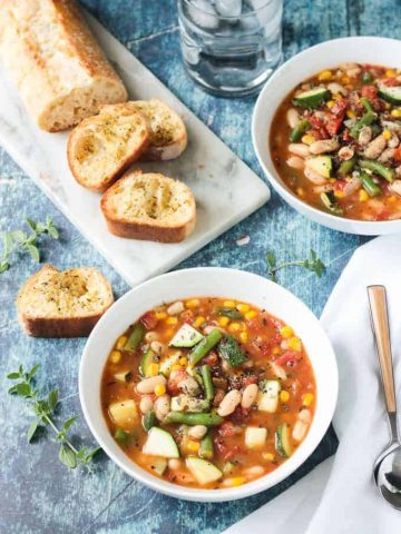 Loaf of sliced bread behind a bowl of summer white bean vegetable stew.