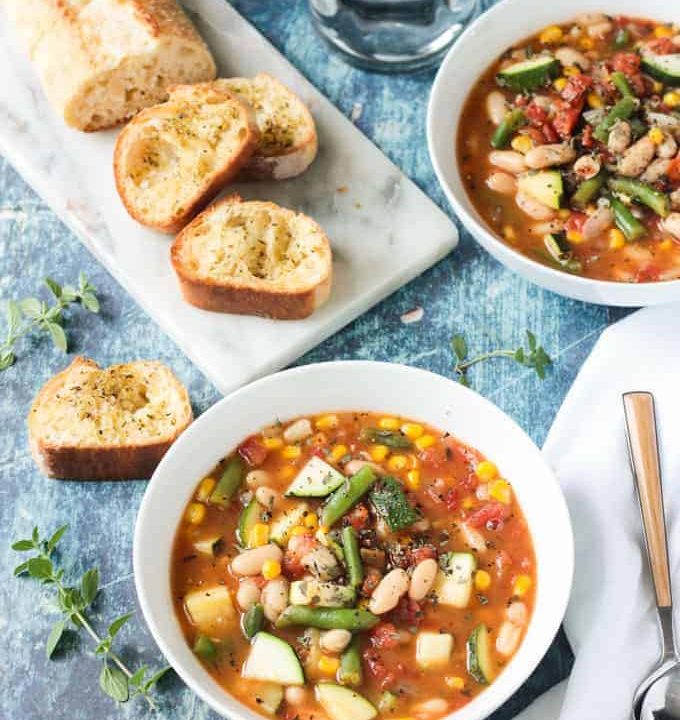 Loaf of sliced bread behind a bowl of summer white bean vegetable stew.