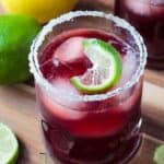 Glass of cherry lemonade garnished with ice and a twisted lime wedge.