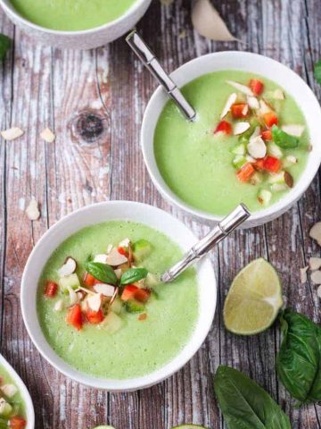 Two bowls of cold cucumber soup with silver metal spoons in them.