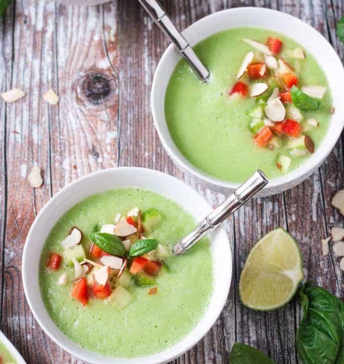 Two bowls of cold cucumber soup with silver metal spoons in them.