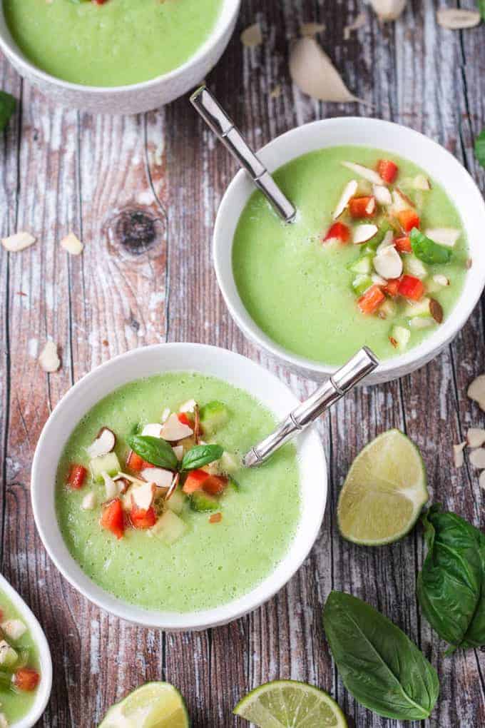 Two bowls of cold cucumber soup with silver metal spoons in them. A lime wedge lies nearby.