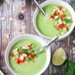 Two bowls of green cucumber soup topped with diced peppers and slivered almonds.