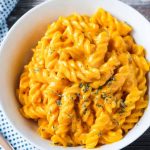 Close up overhead view of a plate of rotini noodles mixed with vegan cheese sauce and sprinkled with parsley.