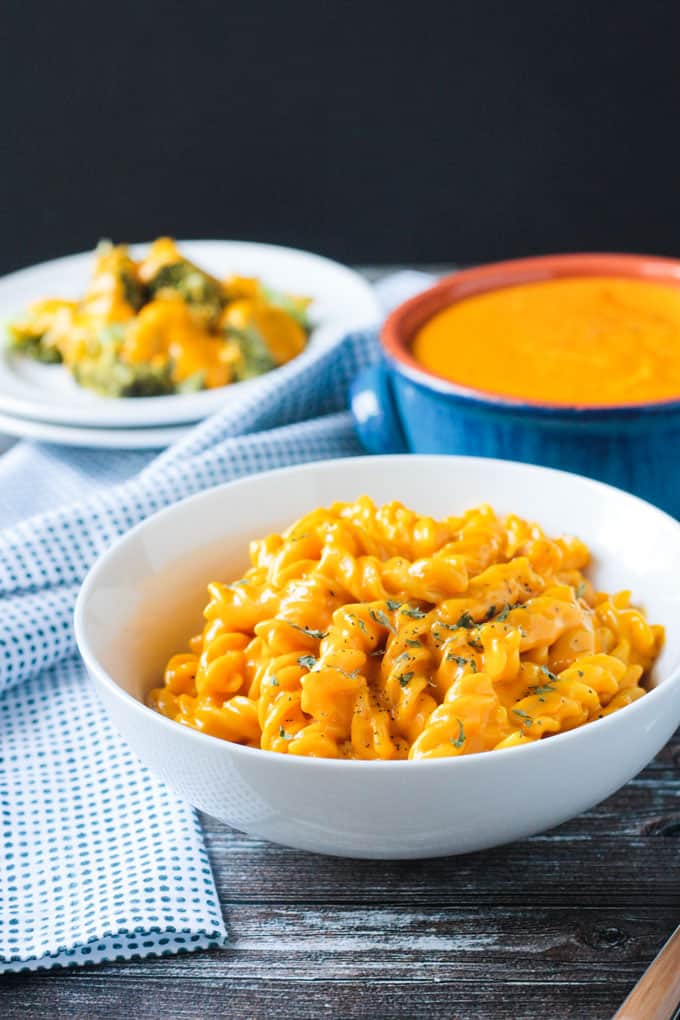 Front view of a bowl of mac and cheese in front of a bowl of vegan cheese sauce.