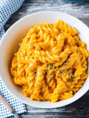 Close up overhead view of a plate of rotini noodles mixed with vegan cheese sauce and sprinkled with parsley.