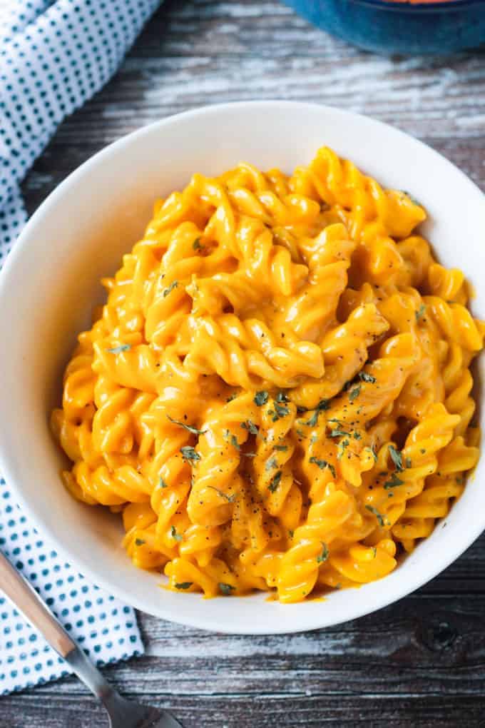 Close up overhead view of a plate of rotini noodles mixed with vegan cheese sauce and sprinkled with parsley.