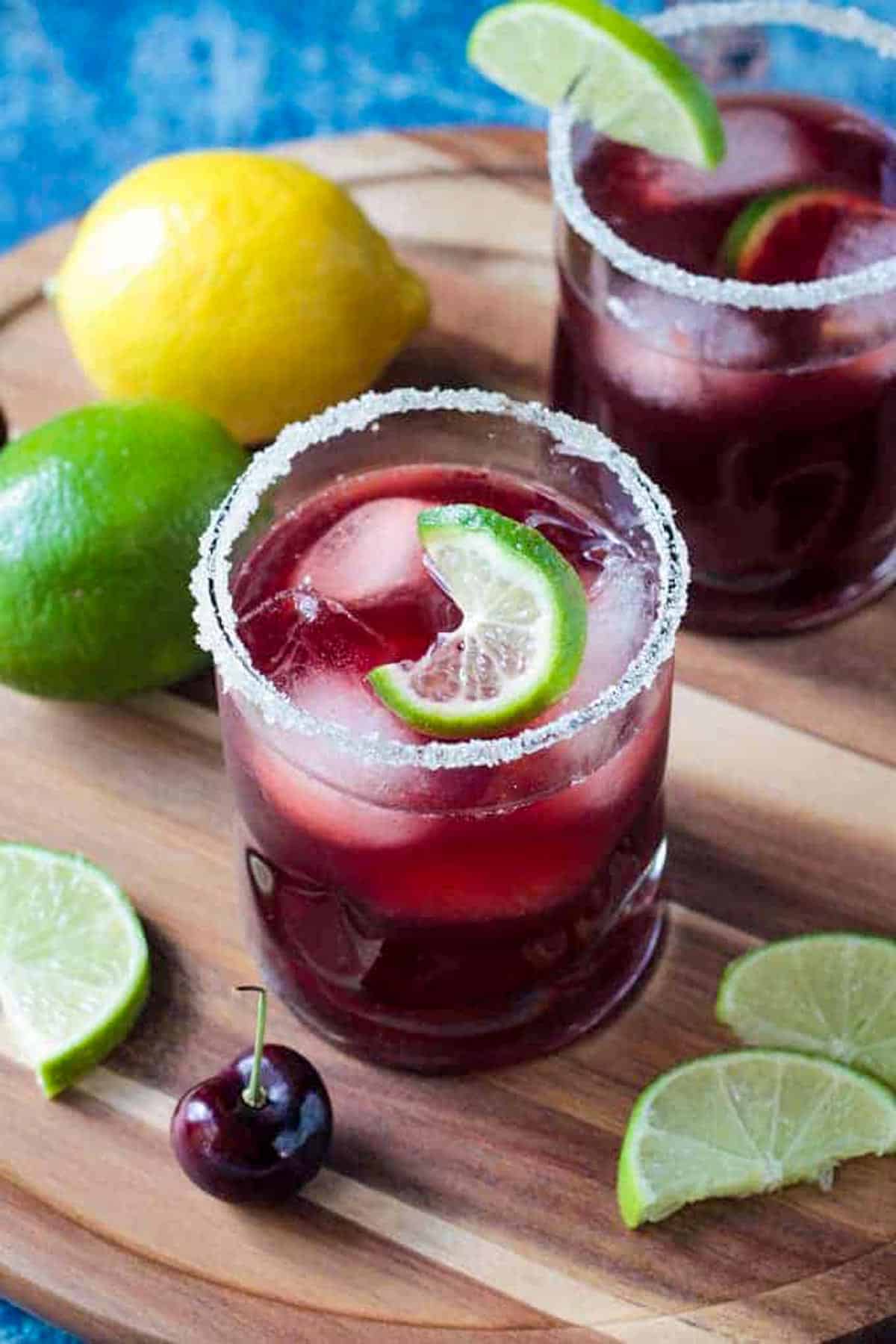 Glass of cherry lemonade garnished with ice and a twisted lime wedge.