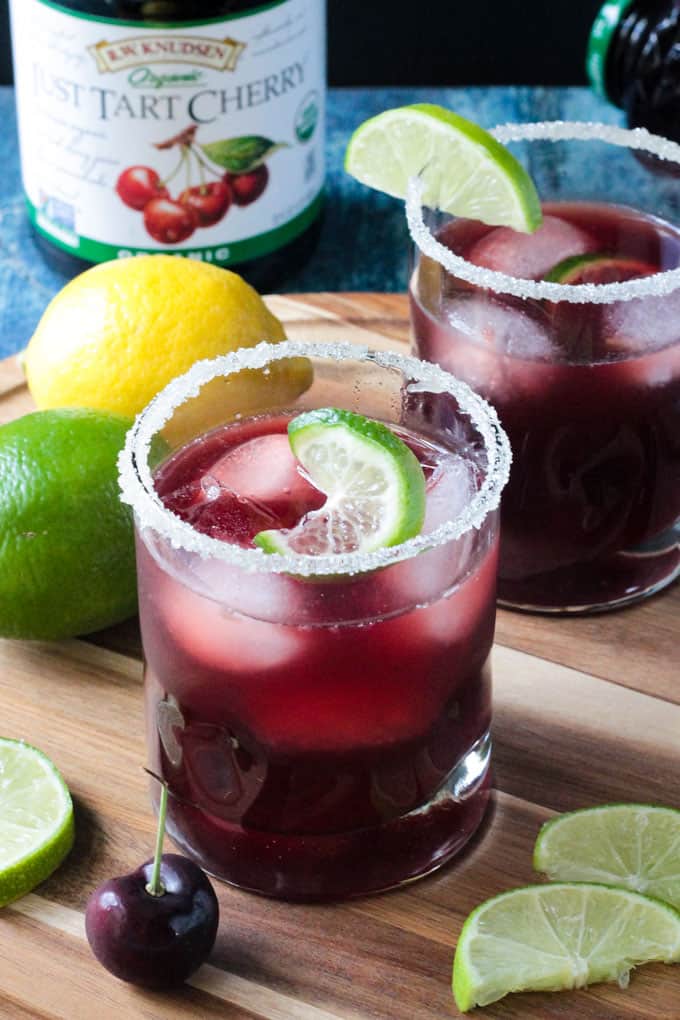 Close up front view of a glass of Tart Cherry Sparkling Lemonade. Fresh lemon and lime in the background.