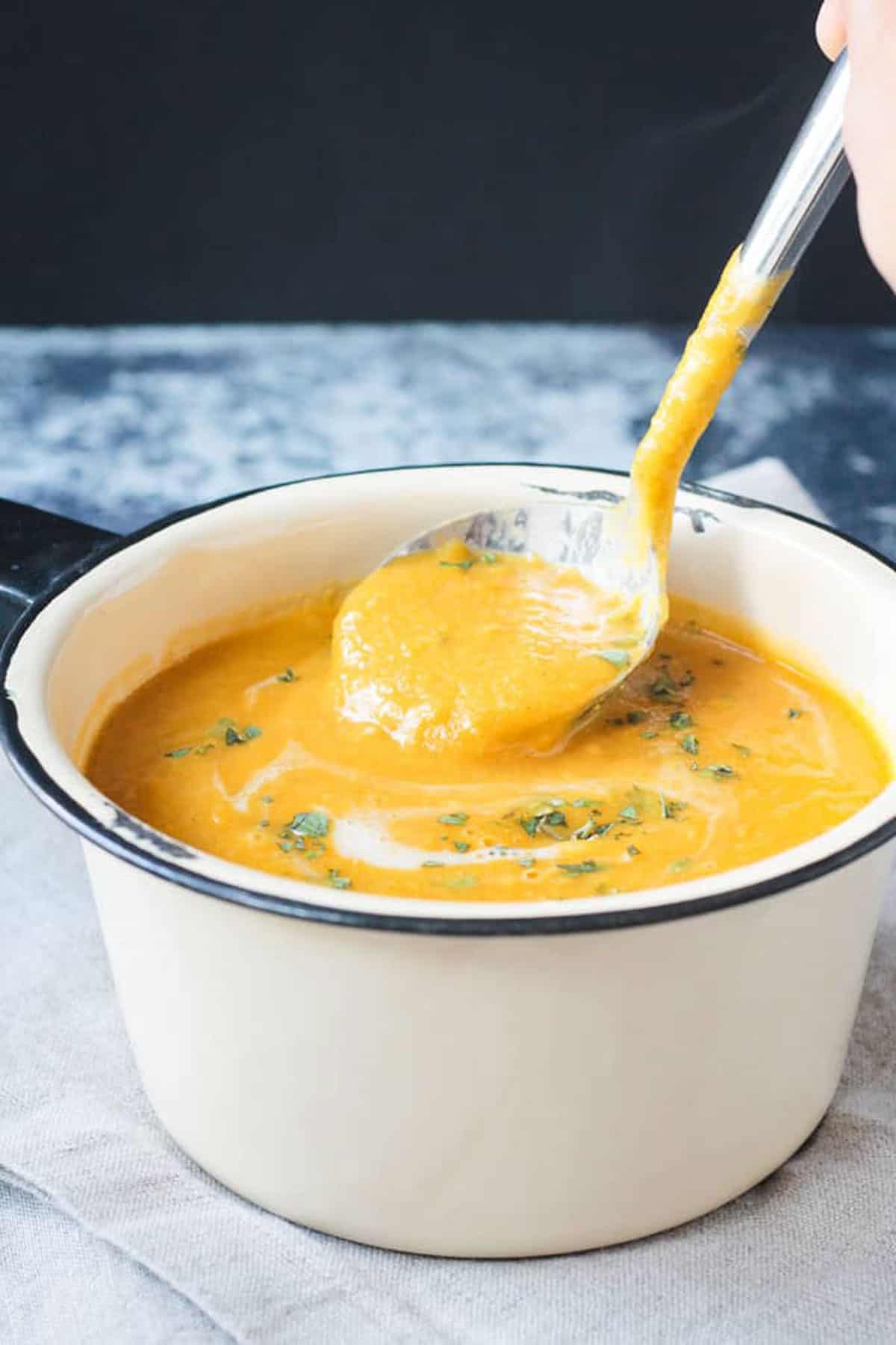 Scoop of vegan butternut squash soup being ladled out of a pot.