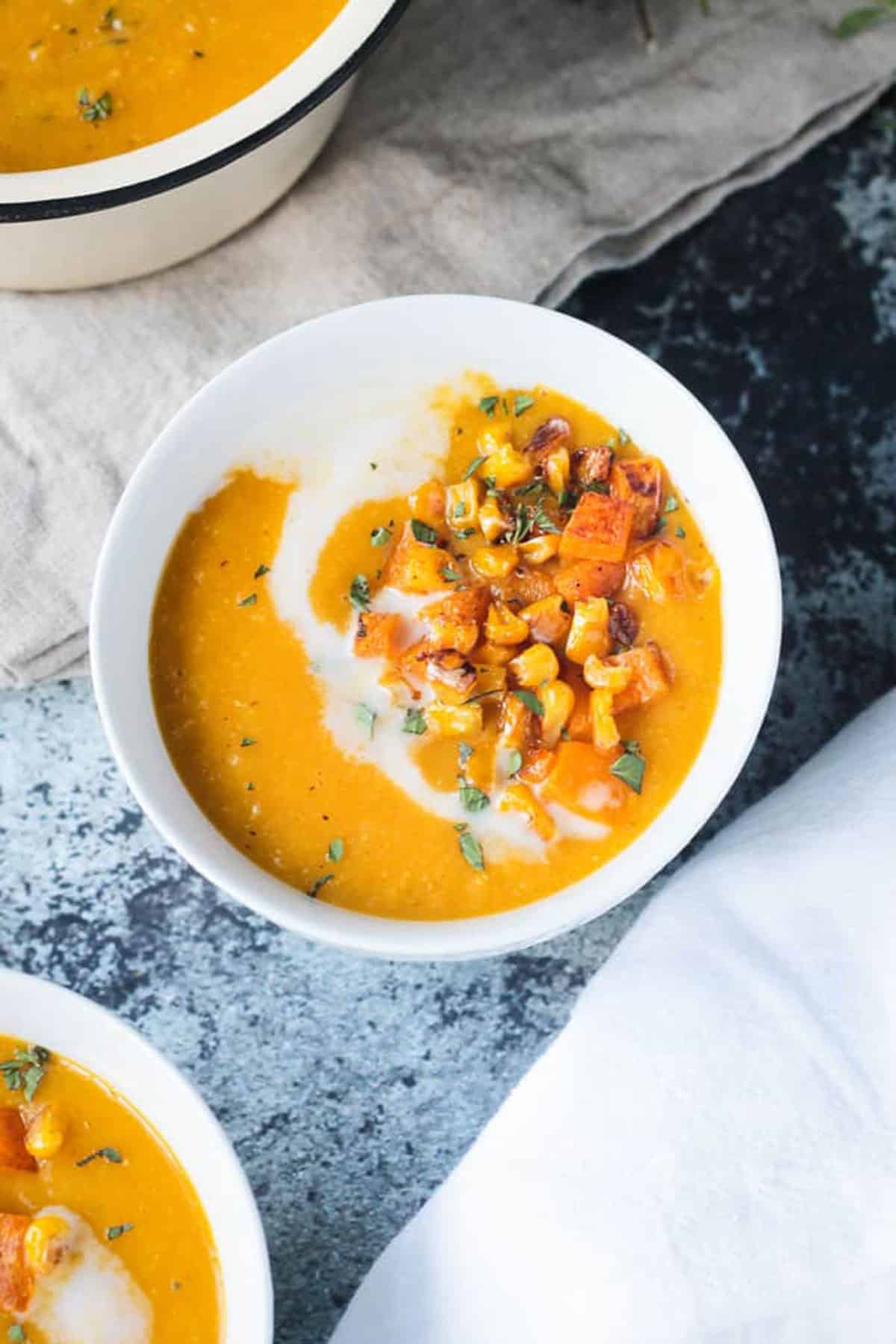 Bowl of vegan butternut squash soup with corn on a slate tabletop with a beige napkin.