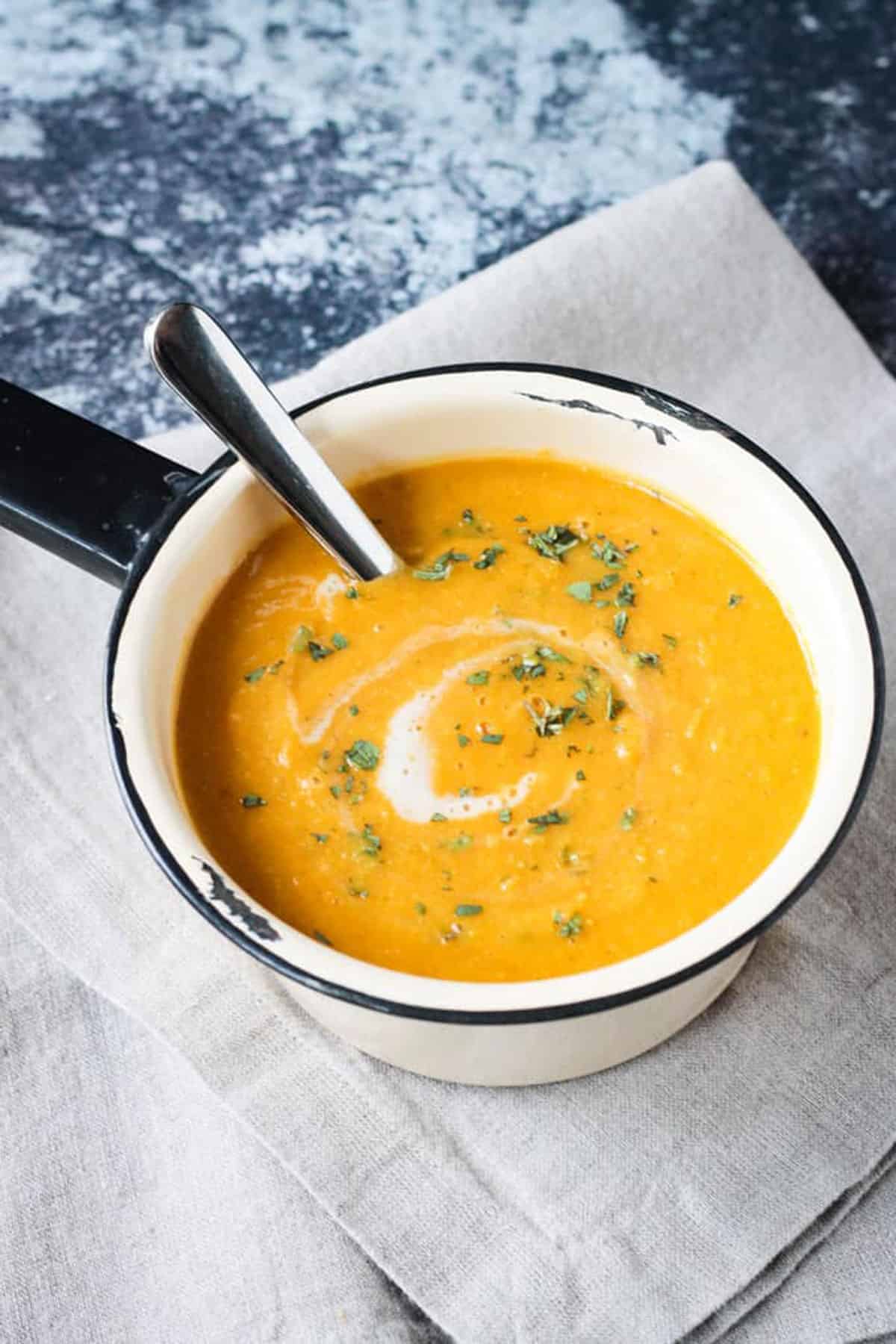 Soup in a small cream colored pot with a black rim and handle. 