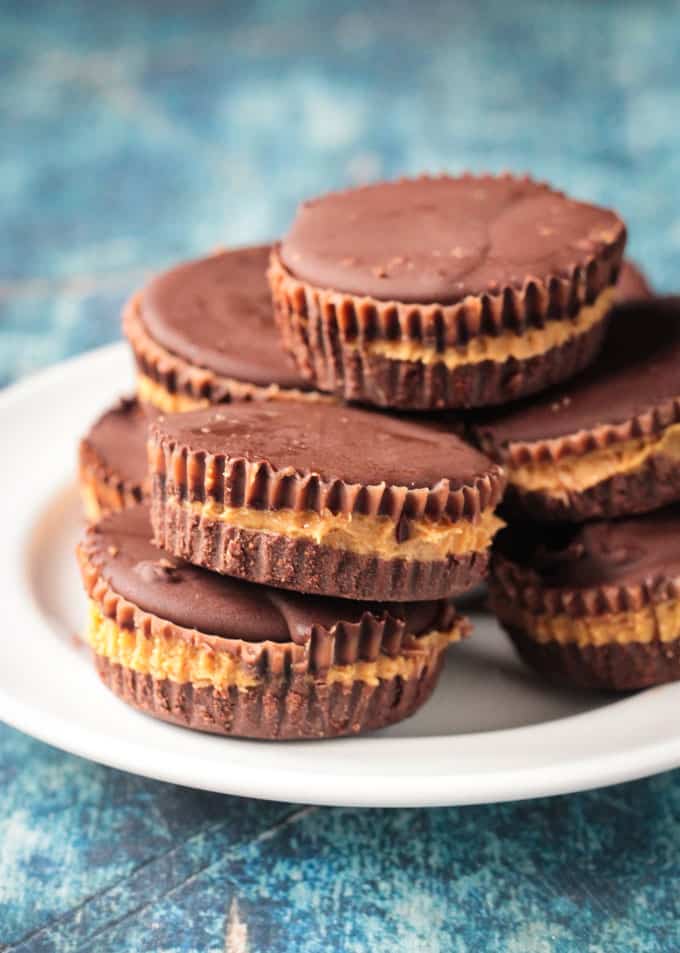 Pile of dark chocolate vegan peanut butter cups on a white plate on a blue background.