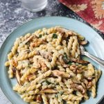 Creamy vegan mushroom pasta recipe on a blue pottery plate topped with toasted walnuts.