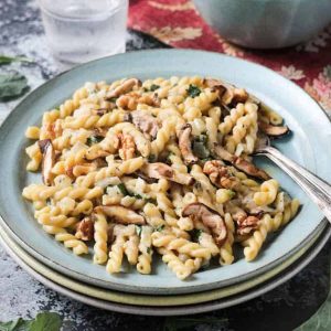 Plate of gemelli pasta with mushrooms in a creamy sauce on a blue plate.