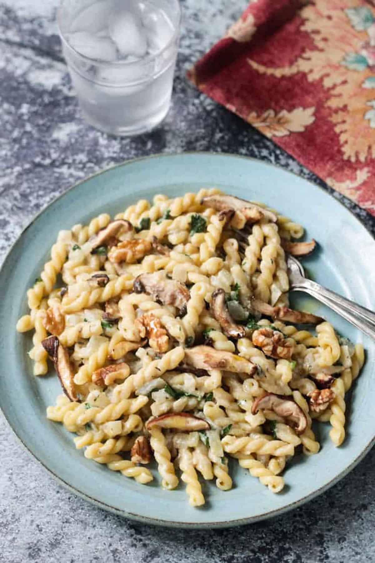 Gemelli pasta with mushrooms and walnuts on a blue plate with two forks.