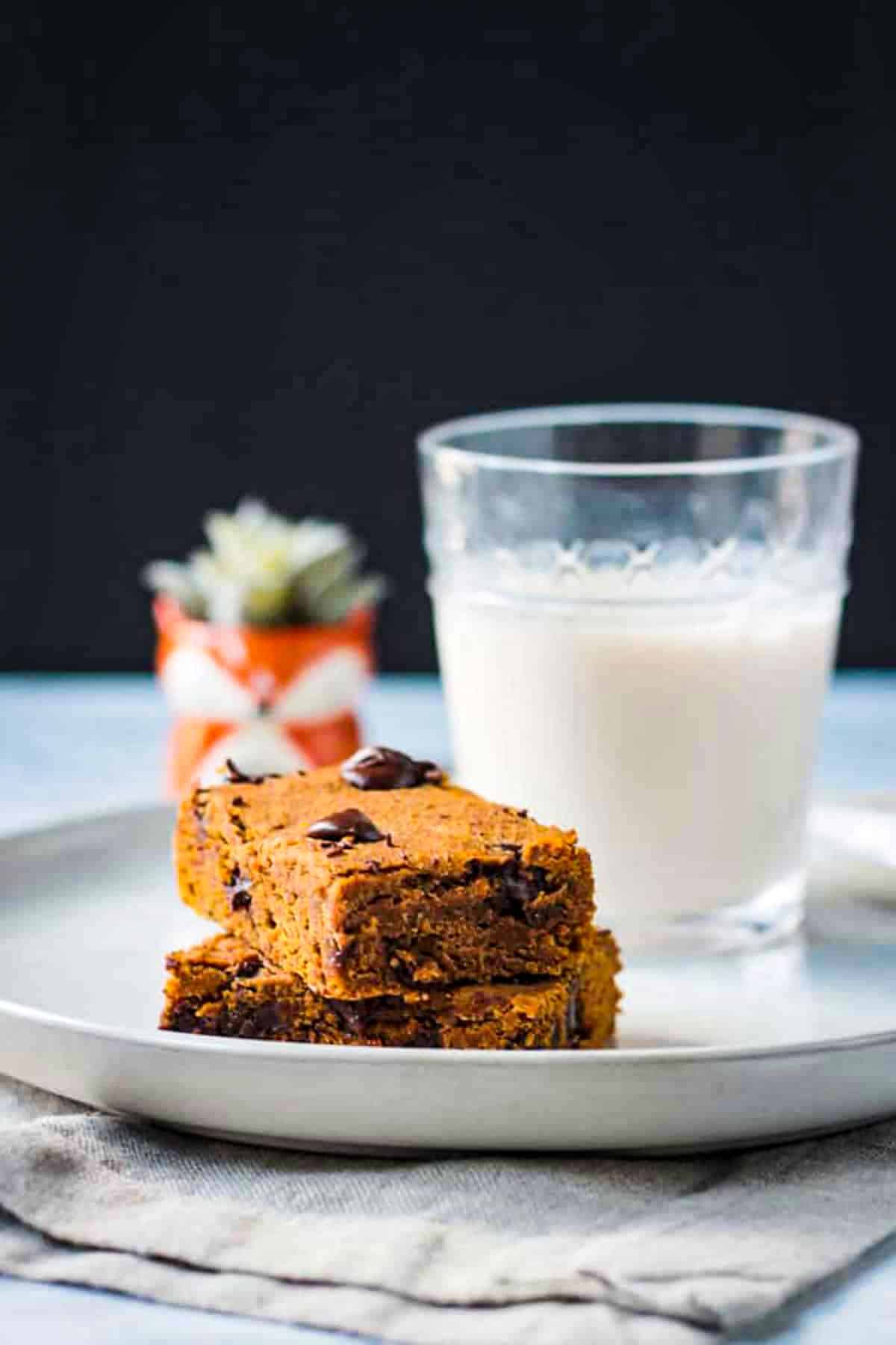 Stack of two pumpkin chocolate chip bars on a plate with a glass of milk.