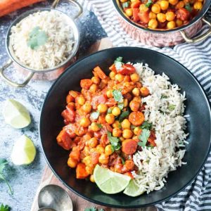 Chunky chickpea vegetable stew next to white rice in a black bowl.