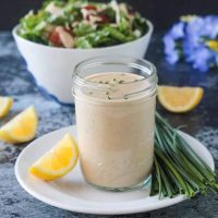 Jar of creamy sauce in front of a bowl of salad.