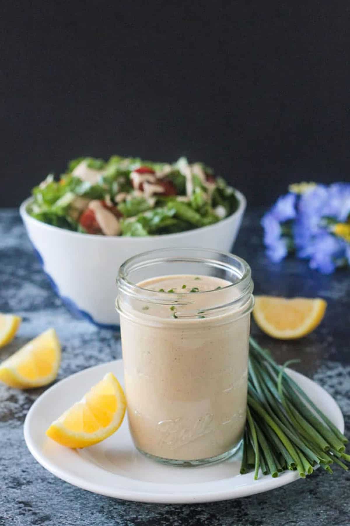 Jar of creamy sauce in front of a bowl of salad.