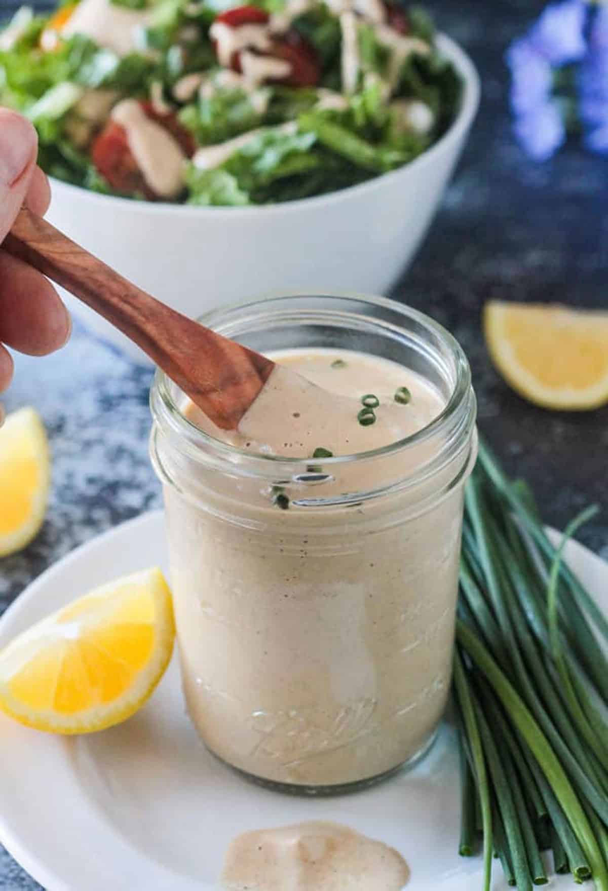 Wooden spoon in a glass jar of vegan ranch dressing.