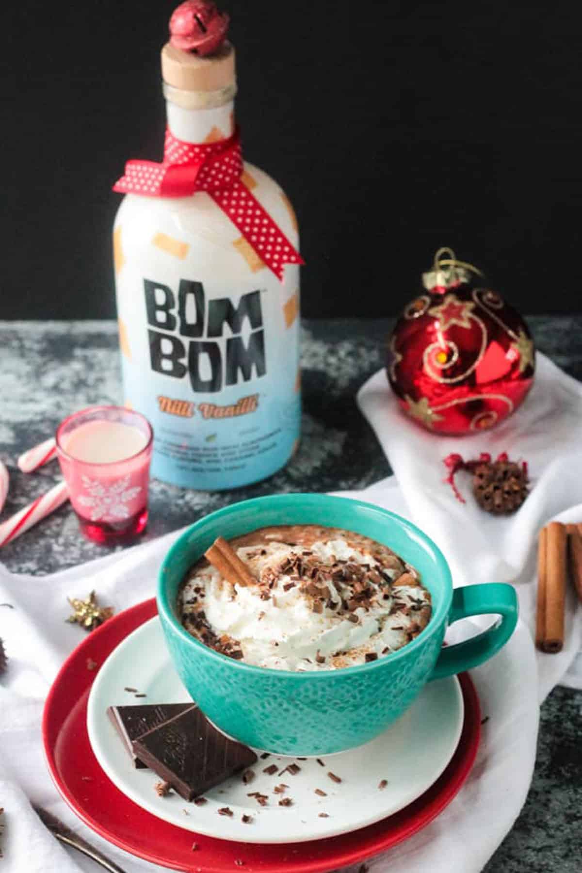 Bottle of Bom Bom almondmilk rum liquor behind a mug of hot chocolate.