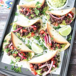 Overhead view of mini tacos on a baking sheet with lime wedges.