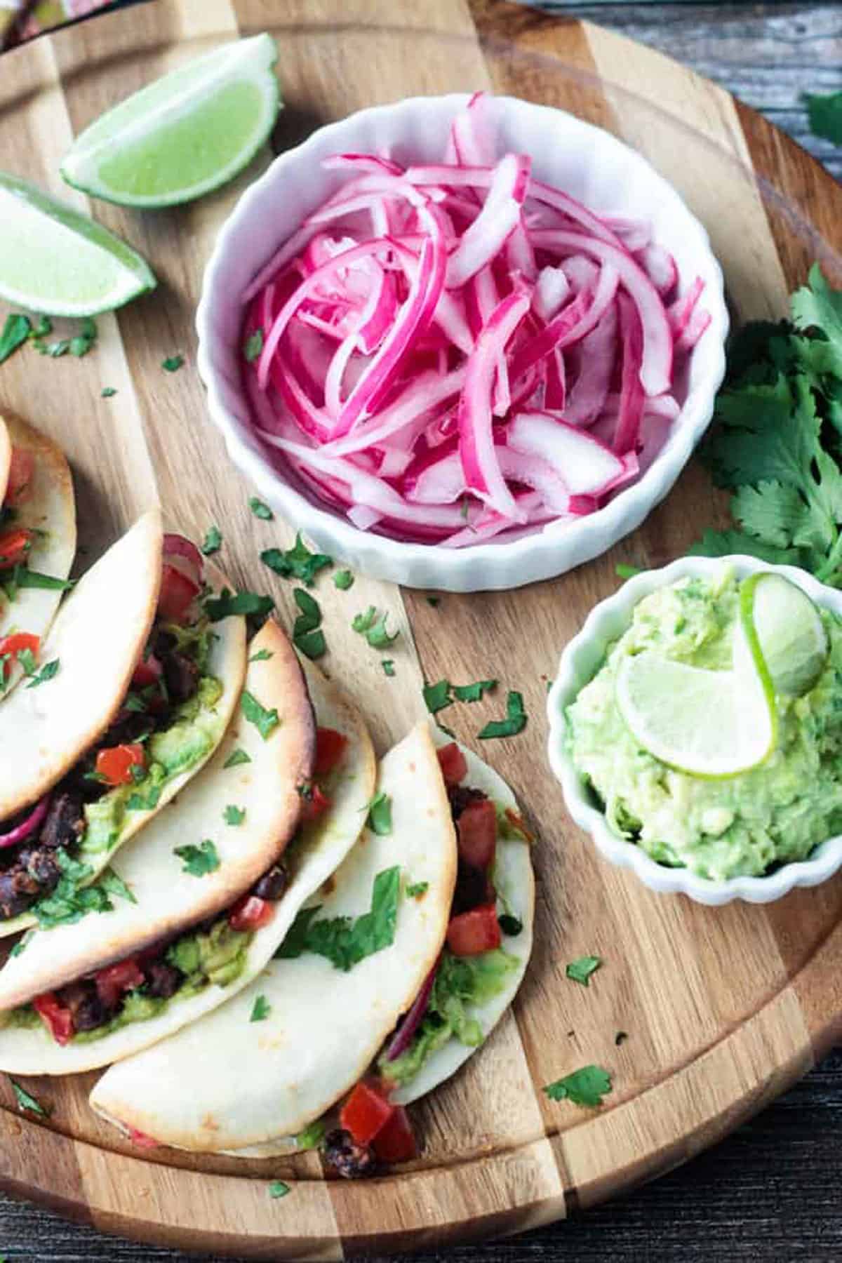 Bowl of pickled red onions in a white bowl next to a tray of tacos.