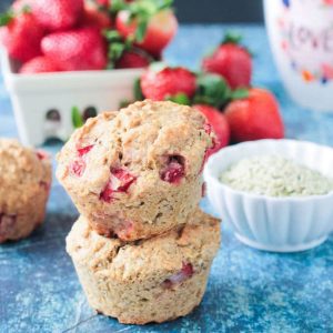 Stack of two strawberry muffins in front of a bowl of fresh strawberries.