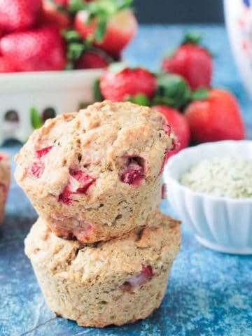 Stack of two strawberry muffins in front of a bowl of fresh strawberries.
