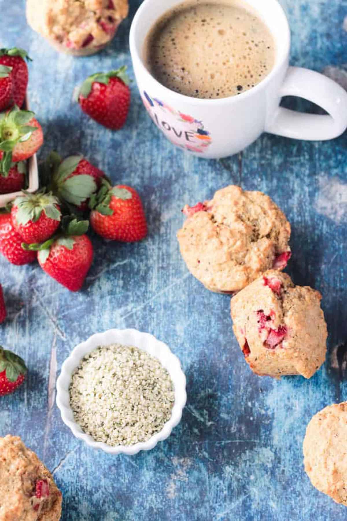 Overhead view of a few muffins on a blue background next to a small bowl of hemp seeds.