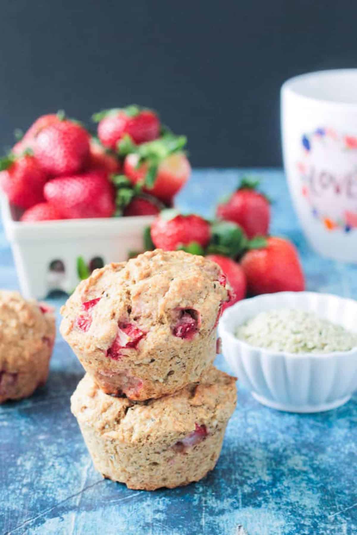 Stack of two strawberry muffins in front of a bowl of fresh strawberries.