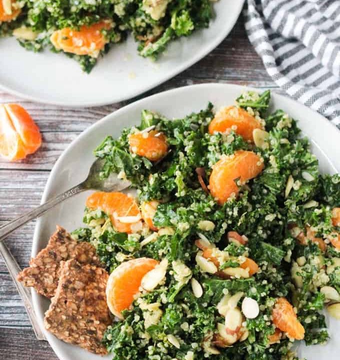Kale and quinoa salad with orange segments and slivered almonds. Two seed and grain crackers on the side.