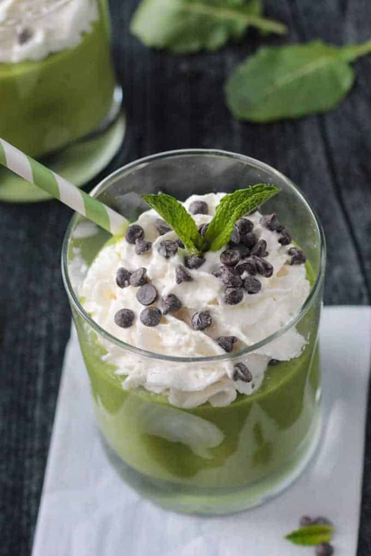 Green smoothie topped with whipped cream, chocolate chips, and a sprig of mint.