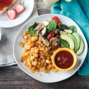 Breakfast plate with hash browns, saut&eacute;ed veggies, and avocado.
