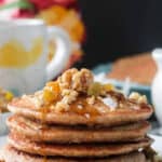 Stack of vegan carrot pancakes topped with walnuts, golden raisins and syrup.