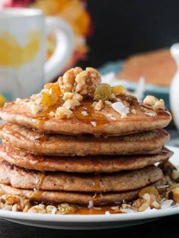 Close up of maple syrup drizzling down the side of a stack of carrot cake pancakes.