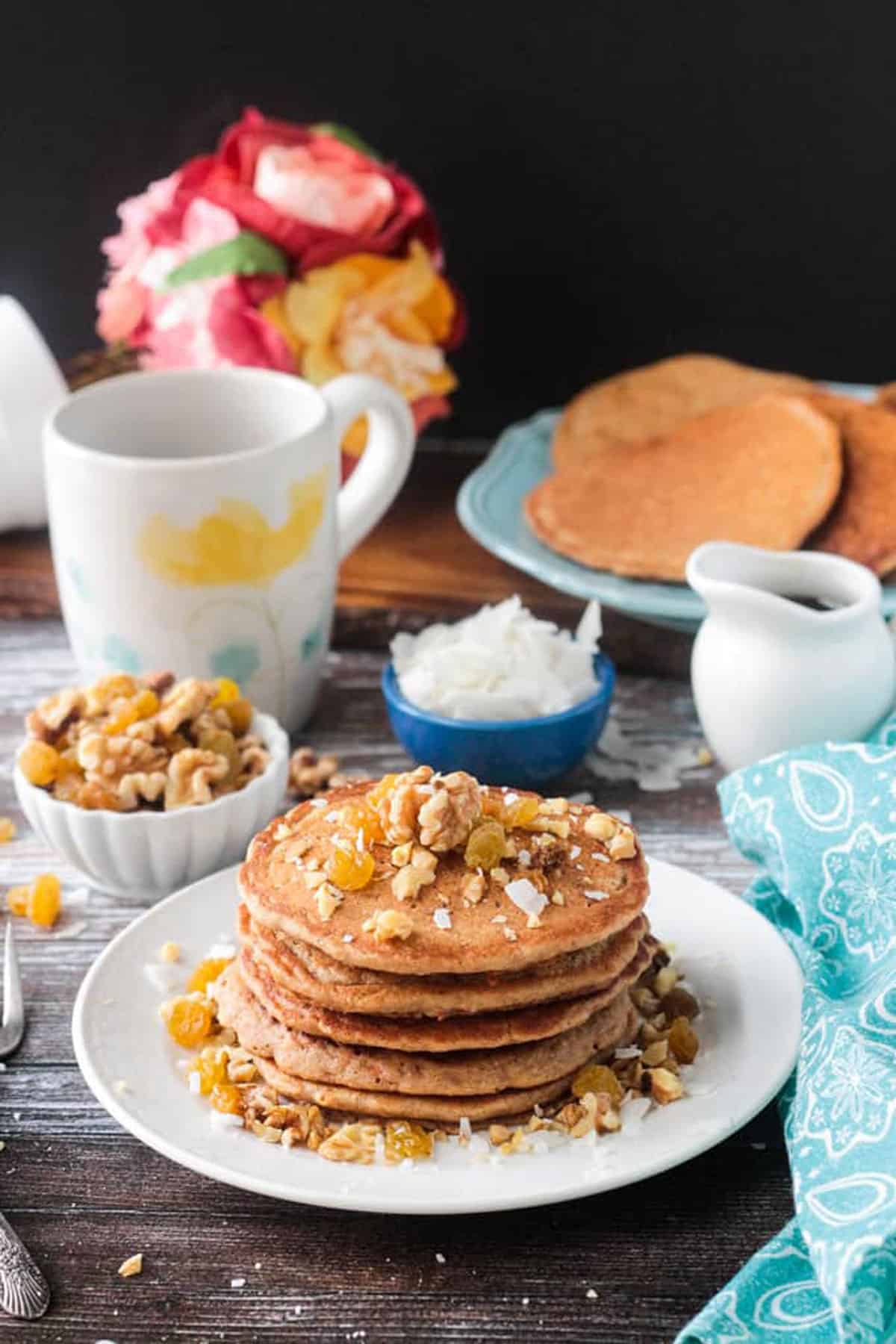 Stack of pancakes on a plate in front of a coffee cup.