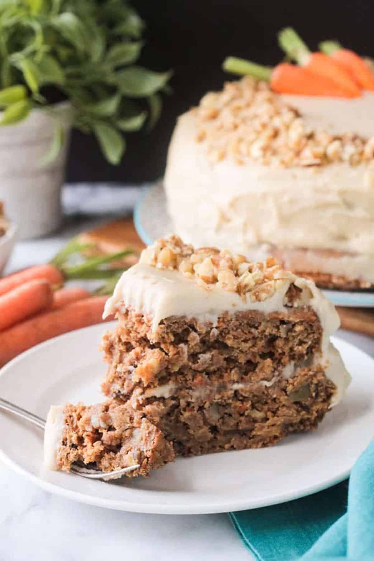 A bite of carrot cake on a fork in front of a slice of cake.