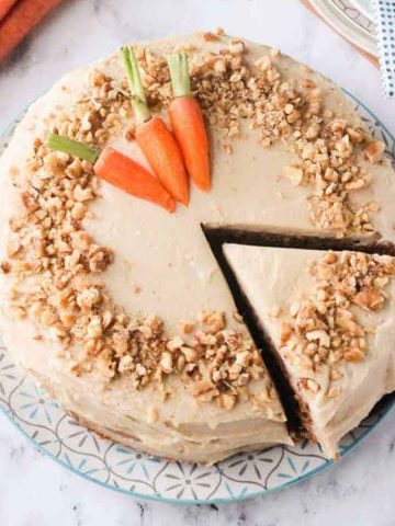 Overhead view of a carrot cake with a slice being taken out with a cake spatula.