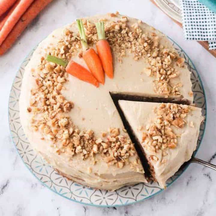 Overhead view of a carrot cake with a slice being taken out with a cake spatula.