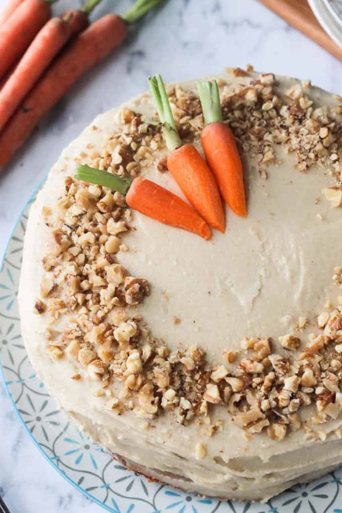 Vegan carrot cake topped with chopped walnuts and three baby carrots.