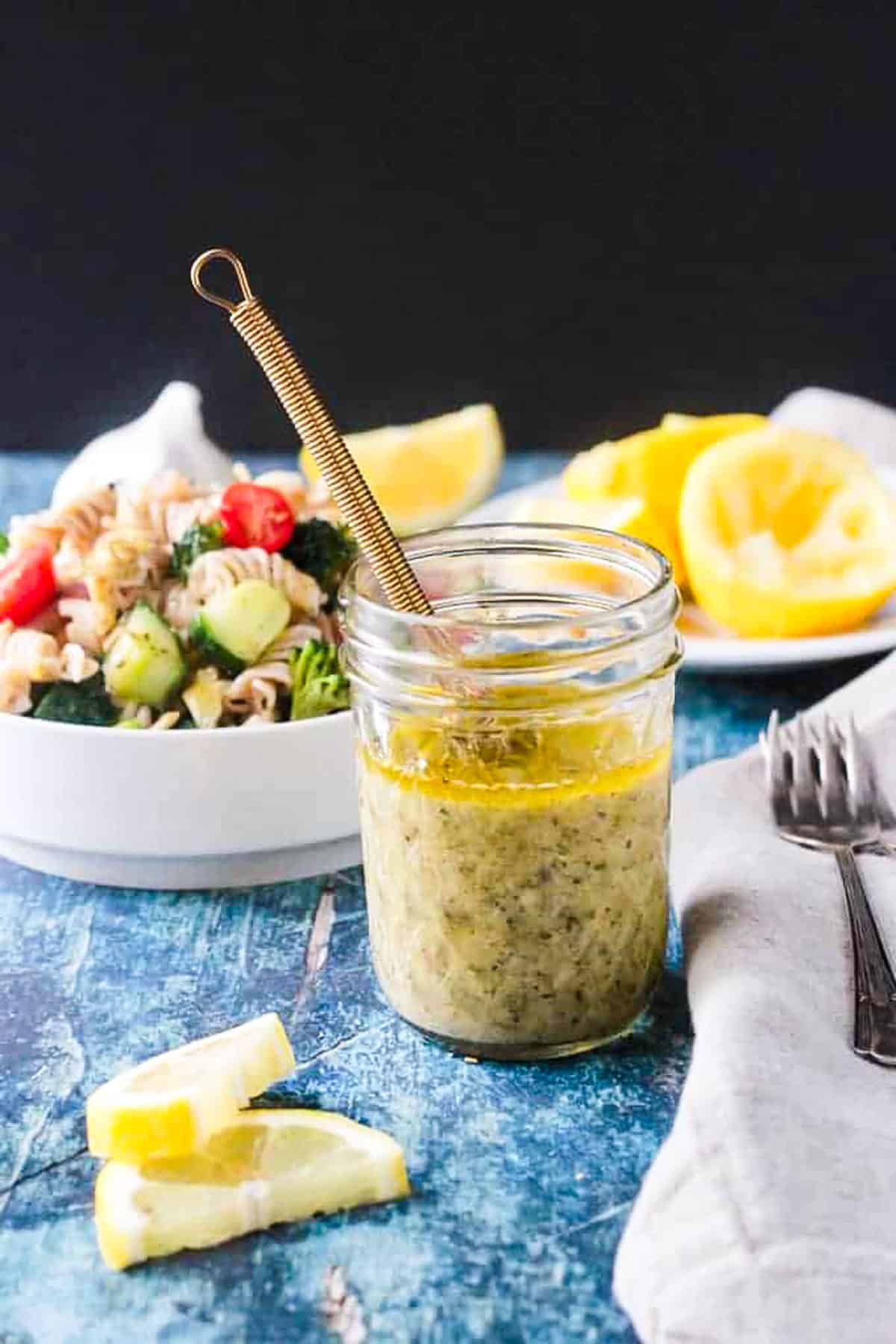 Jar of homemade lemon vinaigrette dressing next to a bowl of pasta salad.