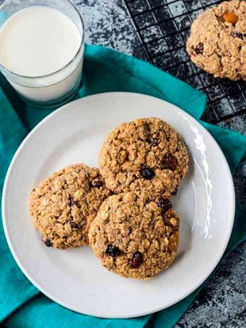 Three oatmeal breakfast cookies on a white plate next to a glass of milk.