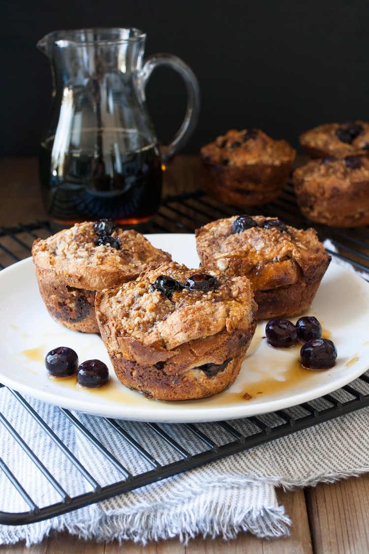 three muffins topped with blueberries on a plate in front of a glass jar of syrup